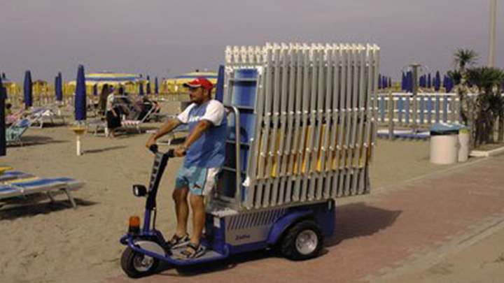 Tractor electrico hombre a bordo JACK L transportando sillas en una playa